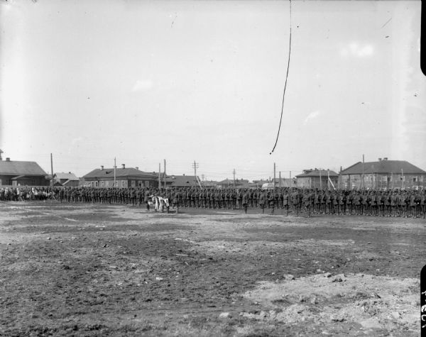 View across grounds towards the British volunteer forces standing review before the Michigan (units) barracks. A group of Russian spectators are watching near the fence in the background on the left.