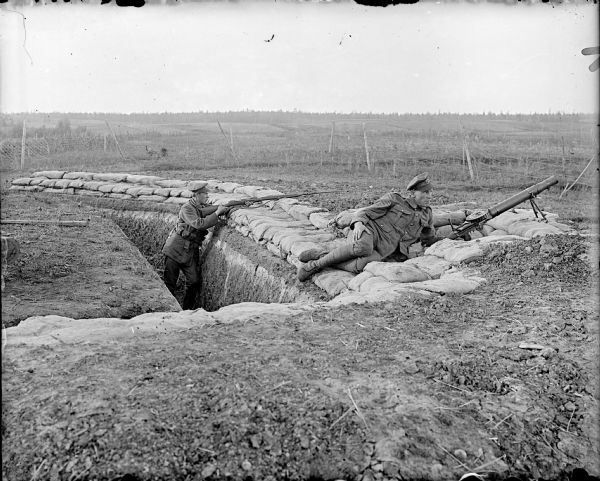Two British soldiers posing in a trench. The soldier on the right is manning an air-cooled Vickers light machine gun, and the soldier on the left is holding a Berthier Fusil Mle 1907/15, a French-built bolt-action rifle.