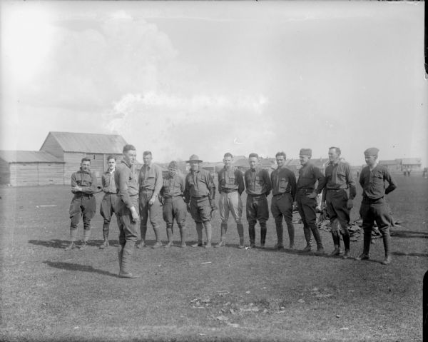 A group of men, possibly from the 310th United States Army Engineer Corps, standing in the drilling field. One of the men is holding a catcher's mitt, and the man standing in front of the group is Major McArdle.