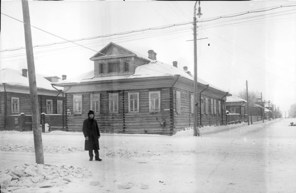 The headquarters building of the 310th United States Army Engineer Corps, showing the street intersection and a man wearing a long coat standing in the snow in front of the building. Power lines or telephone poles are running parallel to the street. One of the poles has a street lamp on top of it. There are other buildings of similar construction, but it is unknown if they are associated with the headquarters building.