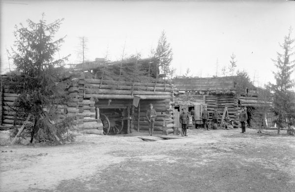 The headquarters and blockhouse of the Unites States Artillery on the Dvina River, showing five uniformed men standing outdoors, and an artillery piece partially concealed within the camouflaged blockhouse. Two of the uniformed men are holding an unidentified rifle.