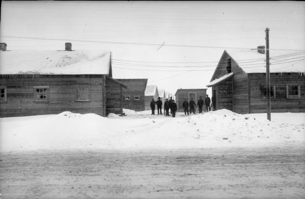 View from snowy road towards a group of men standing among barracks occupied by Army units from Michigan.