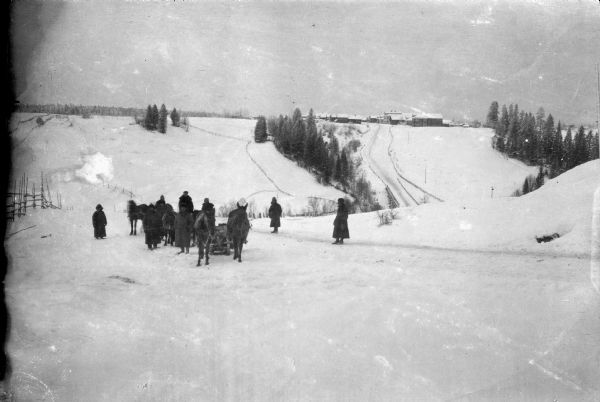 View down snowy hill towards a team of U.S. Army Engineers traveling the Russian countryside in horse-drawn sleighs for the purpose of constructing a map of the section. In the far distance on another hill  is a town with a road leading to it.