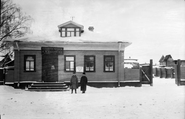 Exterior view of the U.S. Army's YMCA building for those deployed to northern Russia during the Allied intervention there after World War I. The building has a sign in Russian above the entry to the building, and two soldiers are standing in the snow by the front steps.