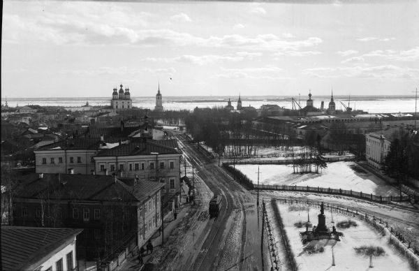 Elevated view of Troitsky prospect in Archangel [Archangelsk], Russia, looking south, showing homes, churches, state buildings, and a statue of Peter the Great. In the distance are some of the cranes near the city's port area.