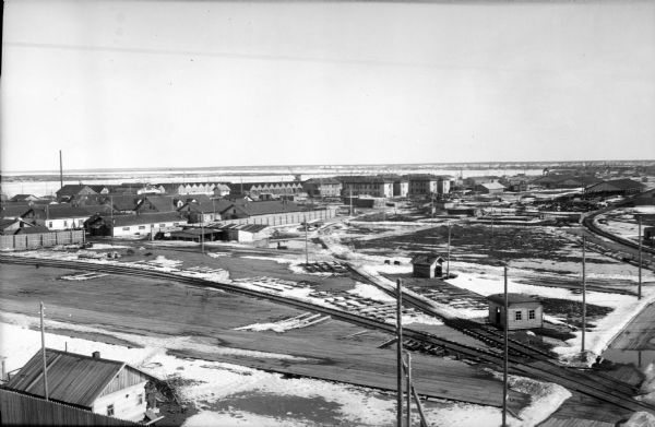 Elevated view of an Allied compound in northern Russia. There are a series of railroad tracks that are leading away from the coast. In the far distance are a number of cranes.