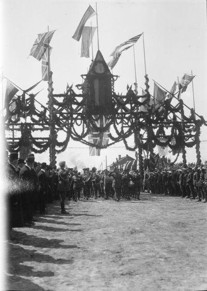 American troops with a band march underneath the "Welcome Arch," while flanked by other sailors and troops.