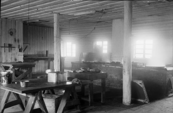 The interior of the kitchen for the United States Army Engineer Corps, 310th Regiment. On the far right side appears to be a brick constructed stove, and thrown about on the wooden tables are skillets, brassiers, pots, and other cooking utensils.