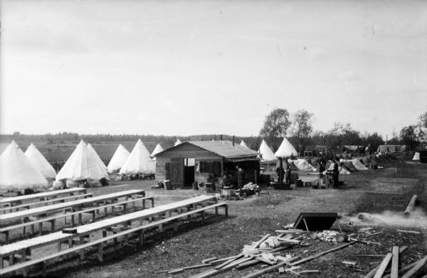 Soldiers standing around portable stoves at the mess hall for American troops. Also shows the bench seated tables and tents used by soldiers.