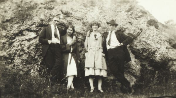 Two couples on an outing, posed in front of an outcropping of rock.
