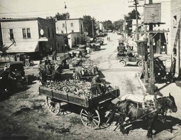 Elevated view of farmers bringing corn to the Lange Canning Co. plant. View looking west, from the west end of the old Madison Street bridge.