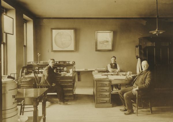 Unidentified railroad station officials, seated at their office desks.