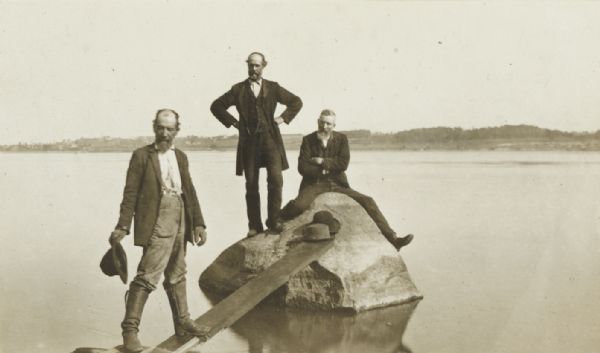 View from shoreline of three men standing in the water at Mechanic's Rock on the Mississippi River.