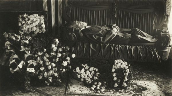 Corpse of an elderly man laid out in his coffin with floral decorations.