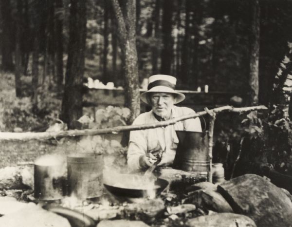 Man cooking over a camp fireplace in a wooded area.