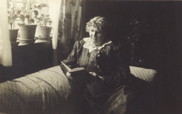 Woman reading, seated on a sofa.