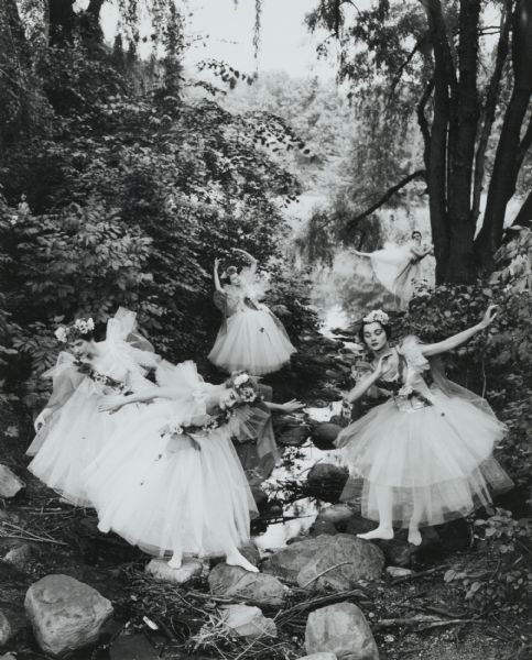 Girls of a visiting ballet company, in costume, posed in a rocky wooded glen along a stream.