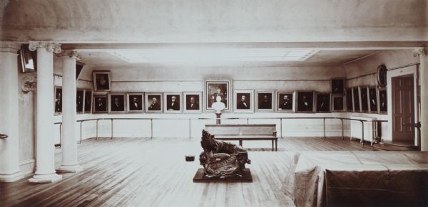 Portrait gallery with paintings in the museum of the State Historical Society of Wisconsin. On the floor is displayed a sculpture of a badger with the word "Forward" at the base.