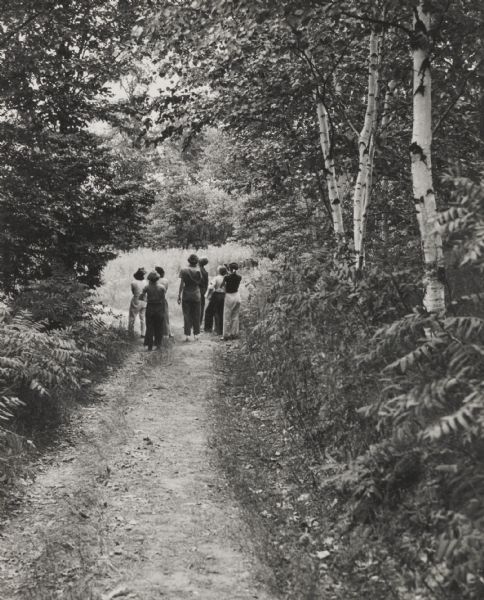 Small group of women with a leader in wooded area on a trail engaged in nature study.