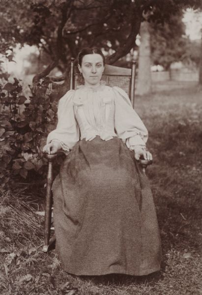 Outdoor portrait of Rose Loomis, of Sullivan, Ohio, wearing a dress and seated in a rocking chair in a garden.