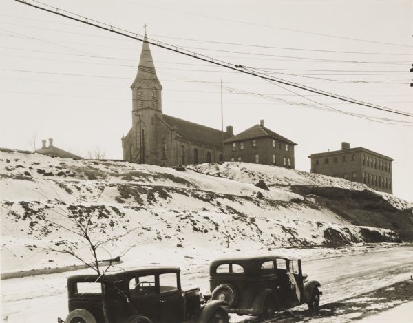 Terracing on Ellis Street during the winter. Two automobiles are parked alongside the road in the foreground. The terraced hill is snow covered, and a church building and other buildings are at the top of the hill.