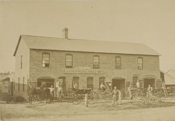 John Parman's “Blacksmith, Wagon & Carriage” shop, with workmen and others posed with vehicles in front.