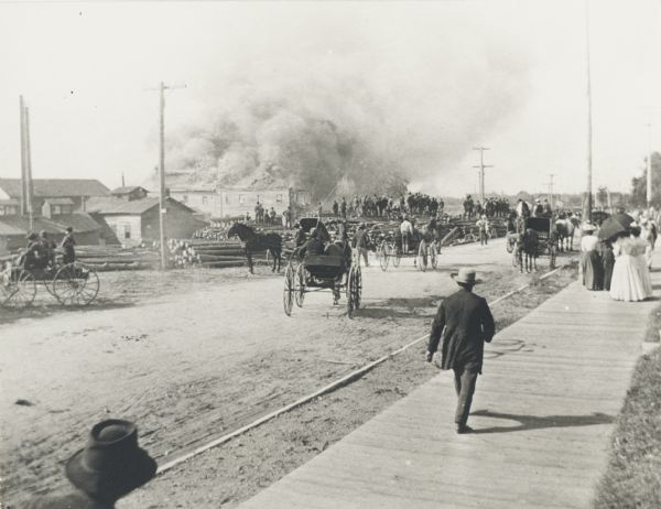 A crowd gathers and watches the sawmill on fire.