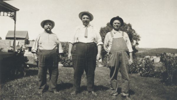Three men standing in a farmhouse yard.