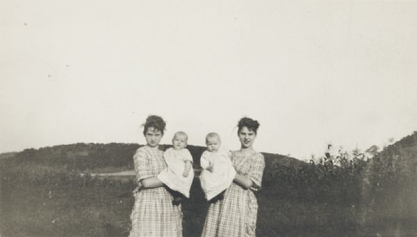 Two young women, each in matching dresses and each holding an infant.
