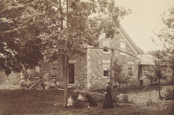 Exterior of a cobblestone house with women and children in the yard.