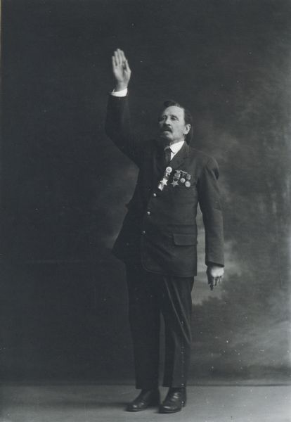 Unidentified man wearing medals, in studio pose apparently as orator, with raised hand.