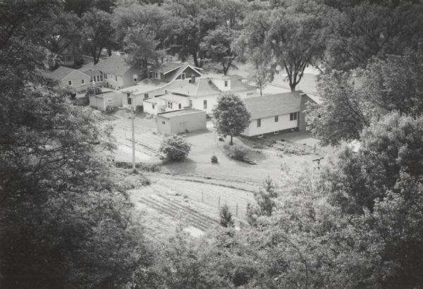 Elevated view from hill of houses and garages surrounded by trees.