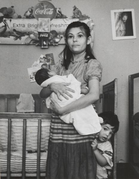 Unidentified young woman in home with small children. Annotated on back: “Victim of recession, Mar. 2, 1958.”
