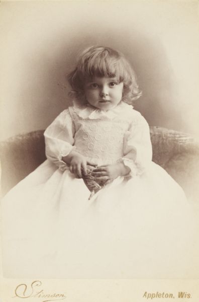 Cabinet posed studio portrait of a young child with a toy in hand and formal dress.