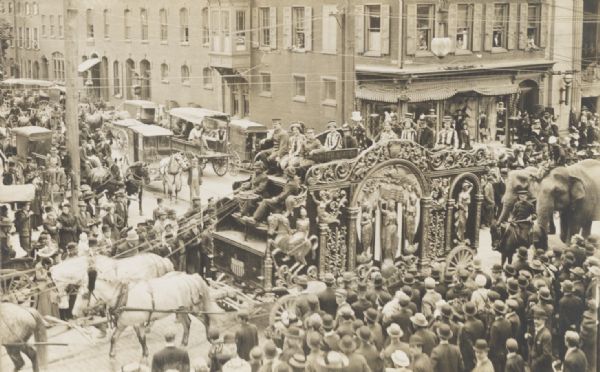 Elevated view of circus parade with "UNITED STATES" tableau wagon passing through a crowded street intersection.