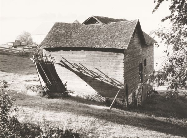 Exterior view of a leaning barn. Shadows from a farm machine fall on the barn's side wall in the early morning.