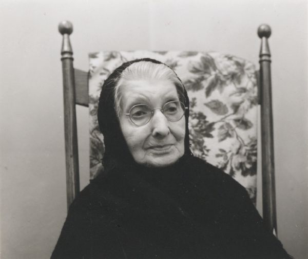 Head and shoulders portrait of an unidentified elderly woman, wearing a shawl, seated in an antique chair.