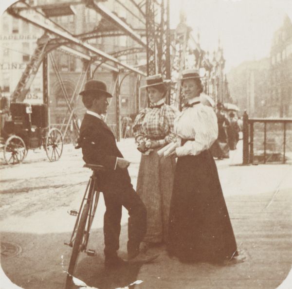 Snapshot of a young man with two young women chatting on Wisconsin Street. The scene is near the Grand Avenue bridge which appears in the background.