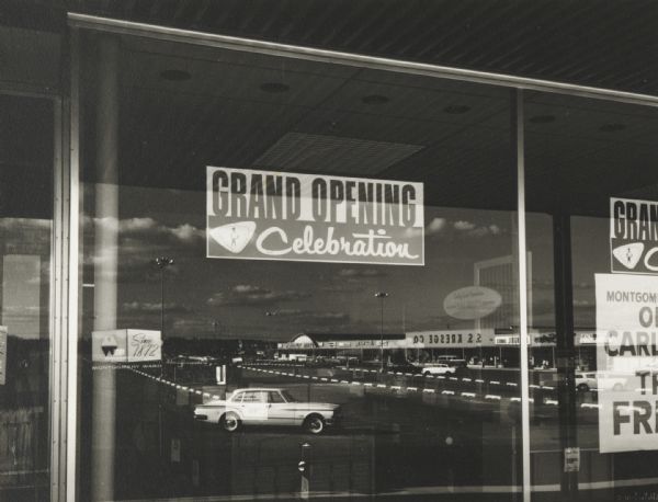 Evening view of the Westgate Shopping Center reflected in Montgomery Ward store window at the time of opening, while the center was still partially under construction.