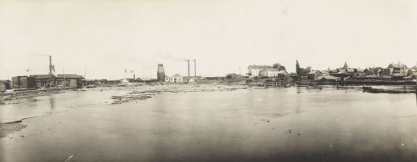 Semi-panoramic view of a river town showing extensive sawmill operations.