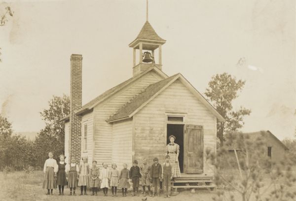 Unidentified one-room country schoolhouse with posed teacher and pupils standing in front.
