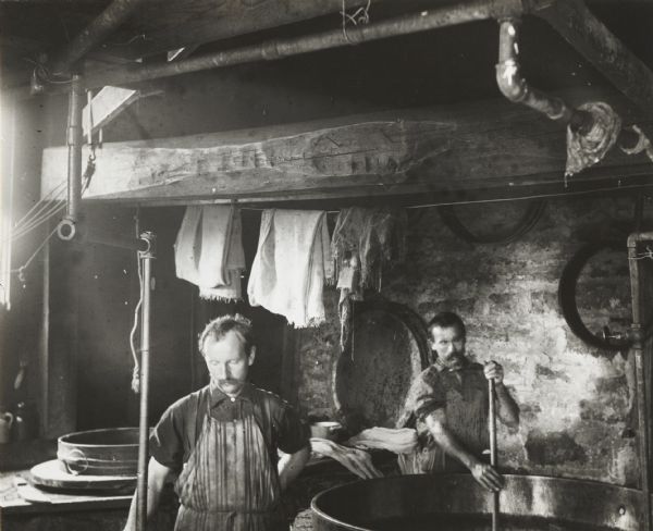 Cheesemakers in a small local factory. The man on the right is stirring a large kettle.
