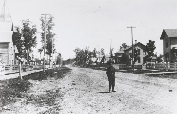 View of Clermont Street with a young boy in the foreground, homes and trees in the background. Fences and sidewalks line both sides of the street.