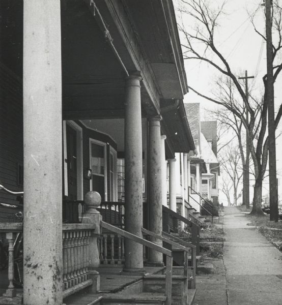 View down sidewalk with the porches of duplex residential houses on the left in the downtown area.
