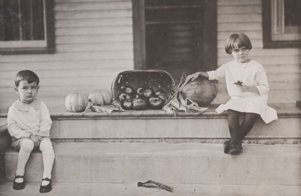 Two children posed on porch steps with assorted garden produce. Probably from the International Harvester Co. Educational Extension Project.