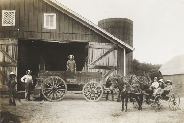 Barn and silo, with horses and farm wagon, and three children in pony buggy. Three men stand near the horse-drawn wagon on the left. The two horses are wearing fly-nets. Probably from the International Harvester Co. Educational Extension Project collection.