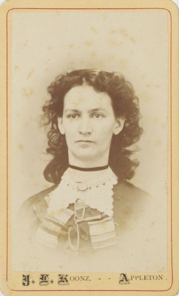 Carte-de-visite quarter-length portrait of an unidentified young woman. She is wearing a lace collar with a brooch, and a dark ribbon around her neck.
