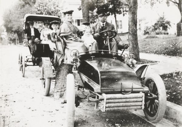 George S. Parker and family seated in their car, one of the first automobiles in Janesville. Behind them is a couple in another car.
