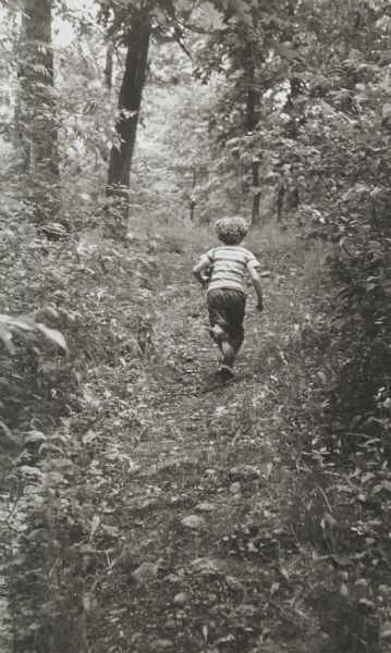Young boy, photographed from behind, running along a wooded path.
