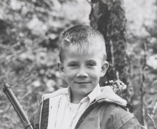 Outdoor informal quarter-length portrait of a boy about 10 or 11-years-old holding a rifle.